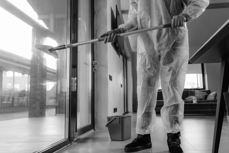 A technician in a protective suit cleaning tall glass doors